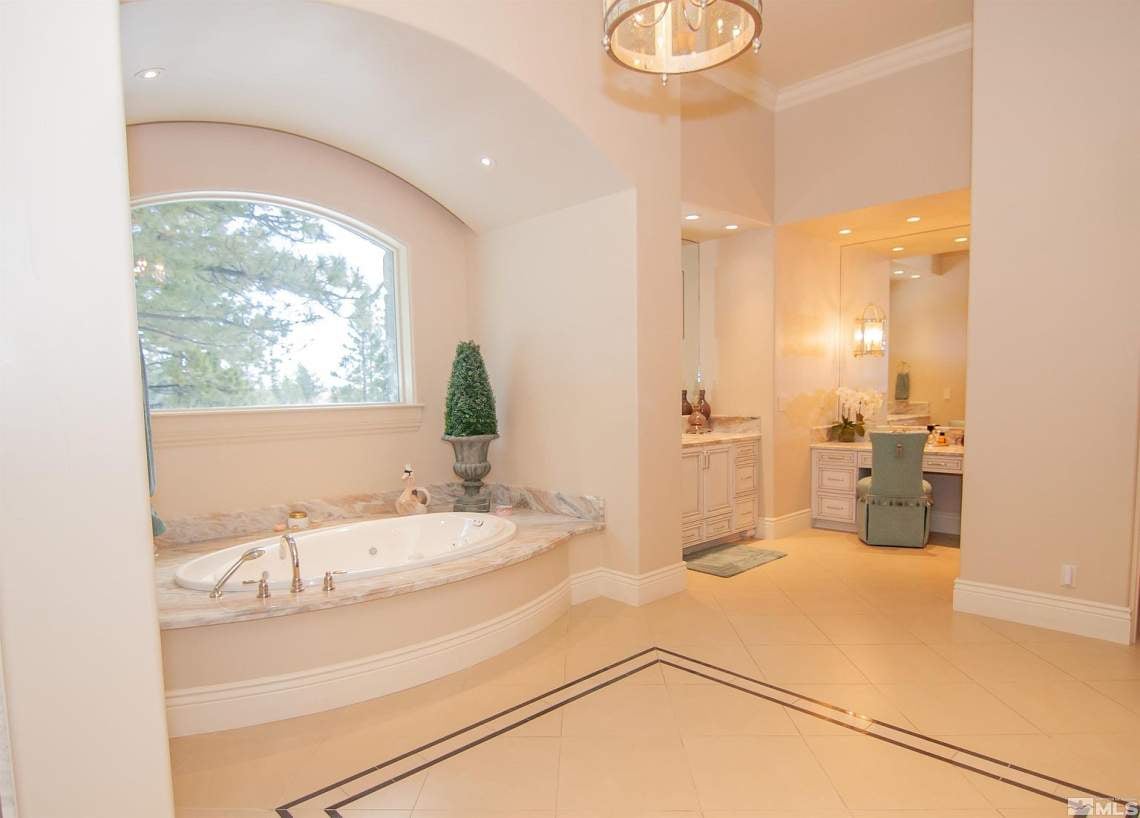Spacious bathroom with a marble-surrounded soaking tub beneath an arched window and an adjoining vanity.