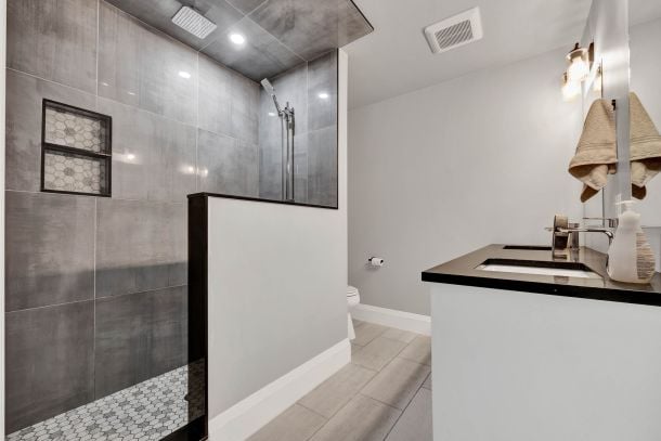 Bathroom with a gray tiled walk-in shower, glass partition, and double-sink vanity.