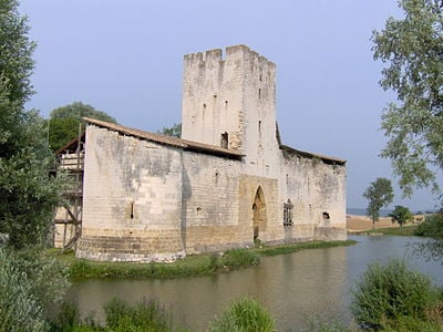 Old stone building with a square tower and arched doorway beside the water.