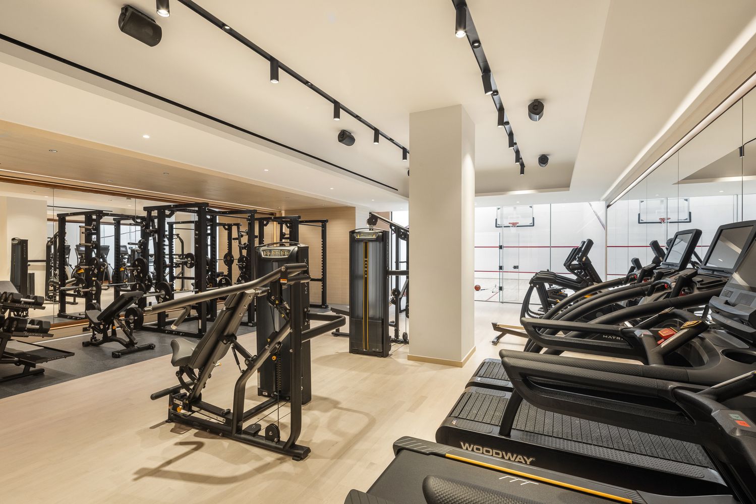 Fitness center with treadmills and weight machines beside a glass-enclosed court.