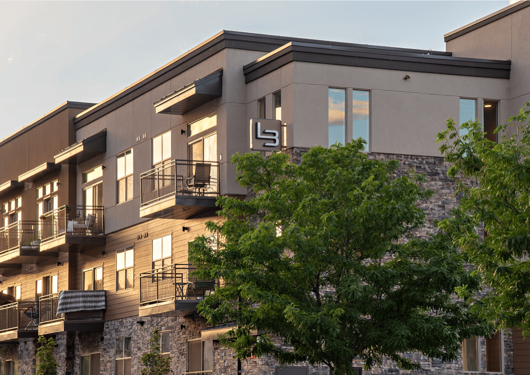 Modern apartment building with balconies, stone accents, and a prominent facade sign.