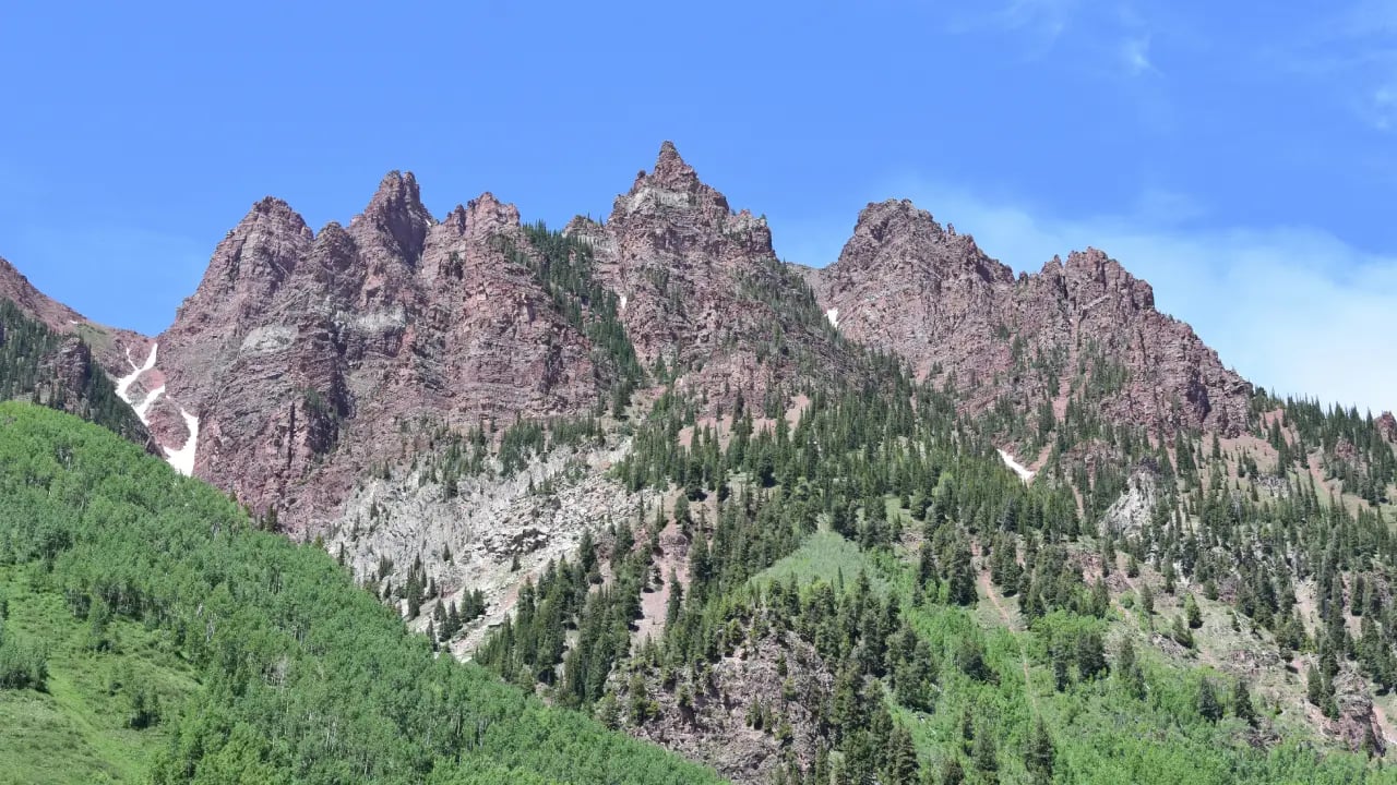Rocky mountain peaks and lush green forest highlight the scenic elevation in Aspen on a bright, clear summer day.