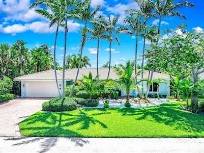 Single-story home framed by tall palms, with a broad driveway and bright green front lawn.