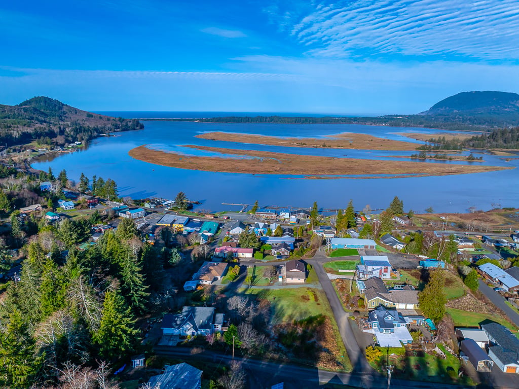 Aerial view of Wheeler, Oregon, overlooking Nehalem Bay, nearby homes, forested hills, and the surrounding coastal landscape.