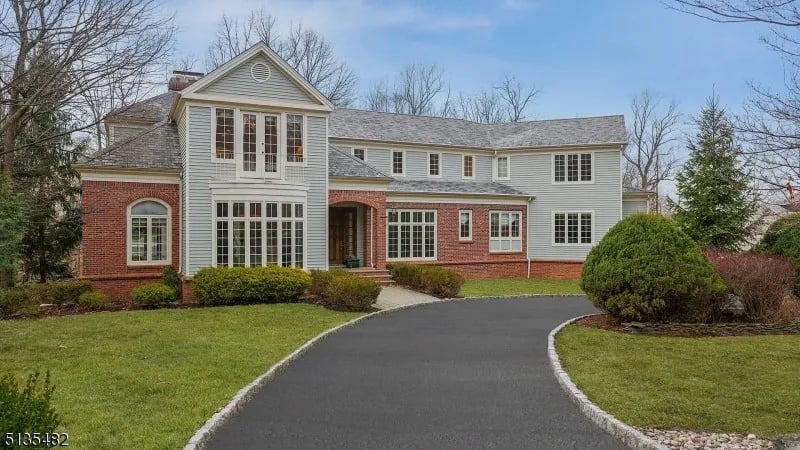 Two-story gray-and-brick home with a curved driveway and landscaped front lawn.