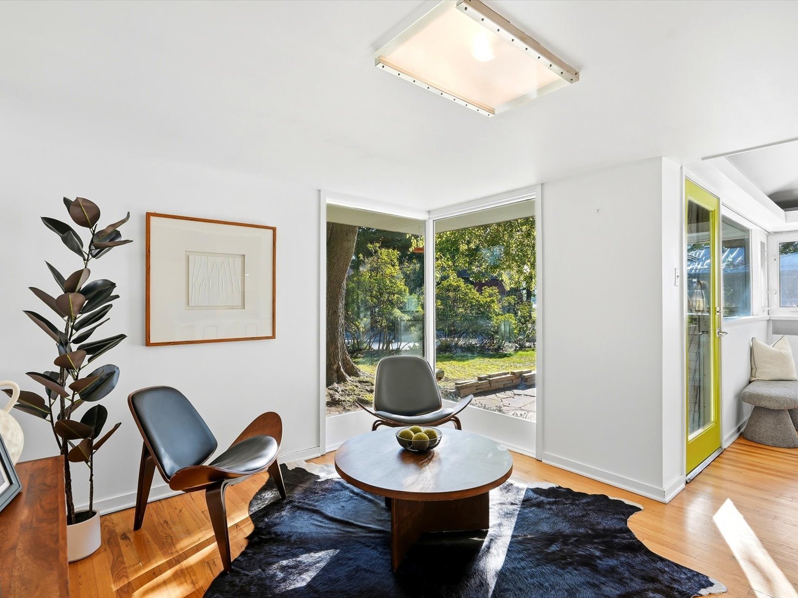 Mid-century modern living room with corner garden windows, sculptural chairs, and a round coffee table.