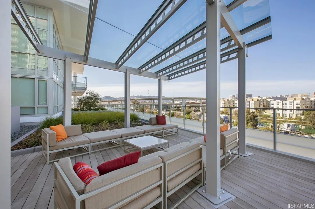 Arden Residences sunny rooftop deck with lounge seating under a glass pergola.