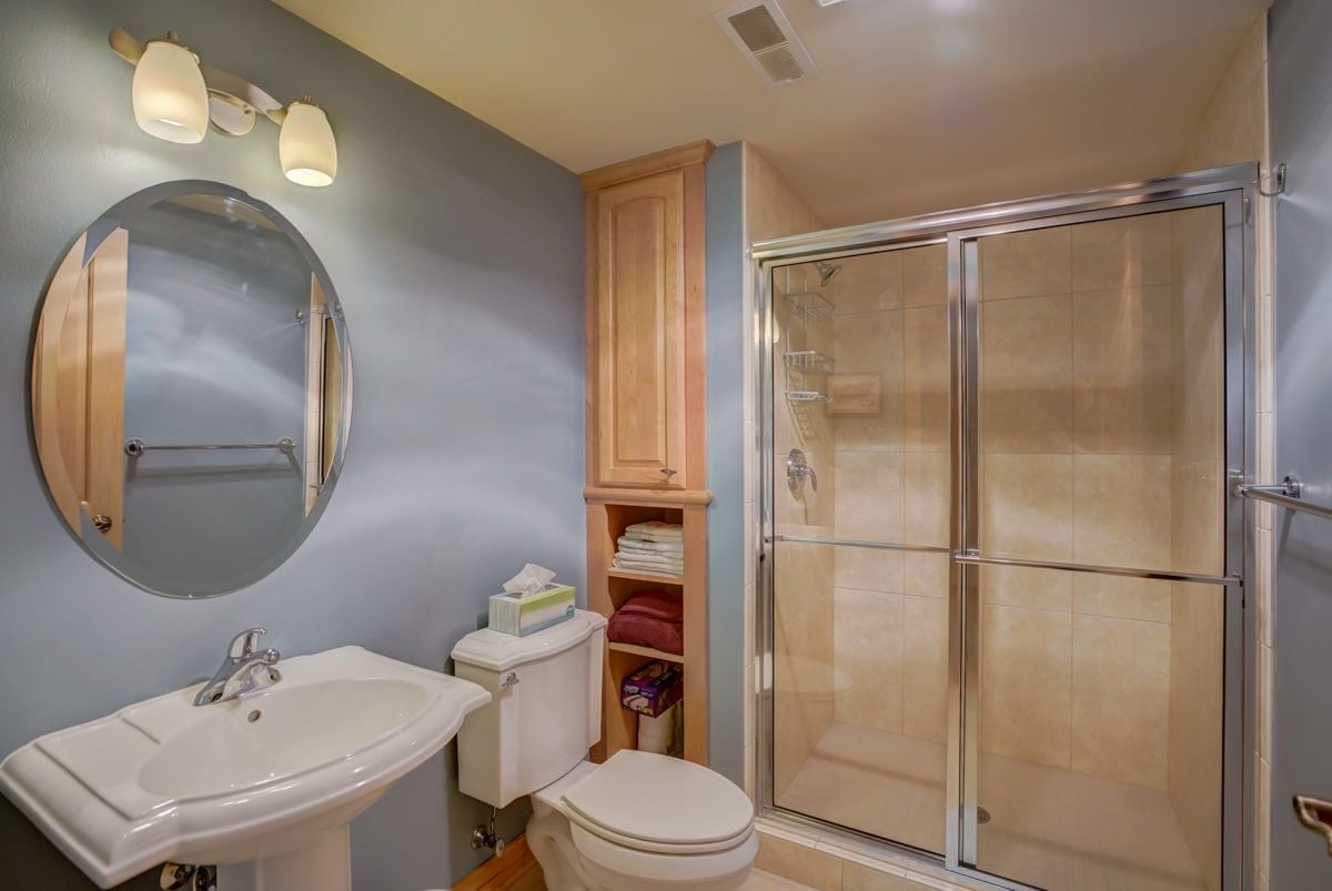 Bathroom with a glass-enclosed shower, pedestal sink, and built-in linen shelves.