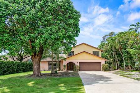 Tan two-story home with an arched entry, brown garage door, and large shade tree.