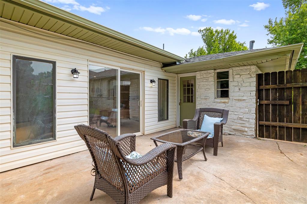 Covered patio with wicker seating beside white siding and a pale stone wall.