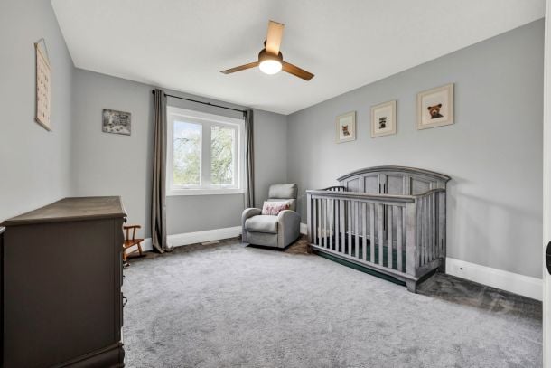 Nursery with a gray crib, armchair, dresser, and window with curtains.
