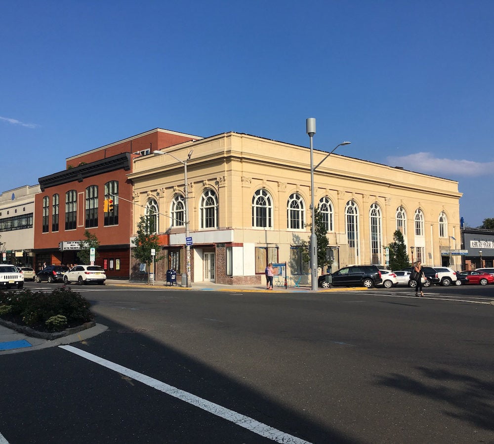 Cream-colored street-corner building with ornate trim and tall arched windows beside a red-brick building.