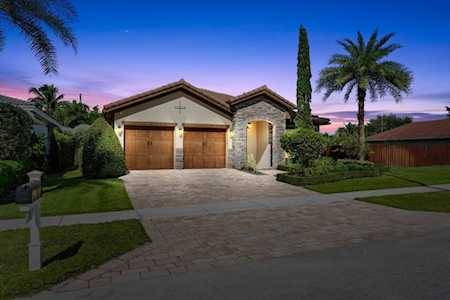 Single-story home with a stone entry, wooden garage doors, and palm trees at dusk.