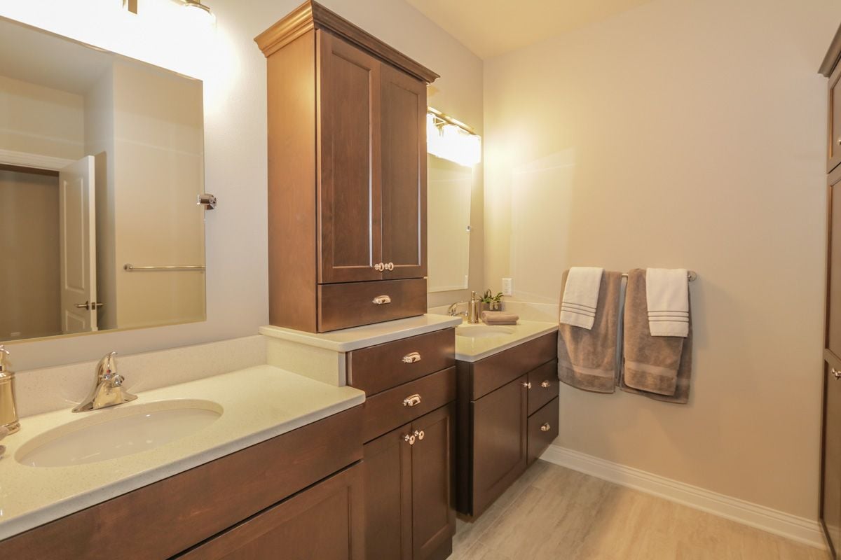 Bathroom with a double vanity, dark wood cabinets, large mirrors, and towels on the wall.