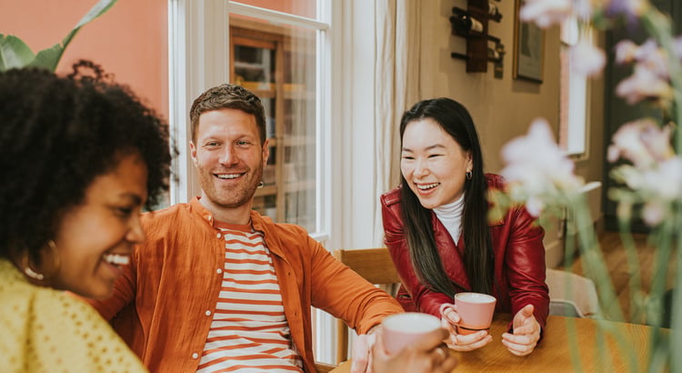 Three adults laughing together over coffee at a café table.