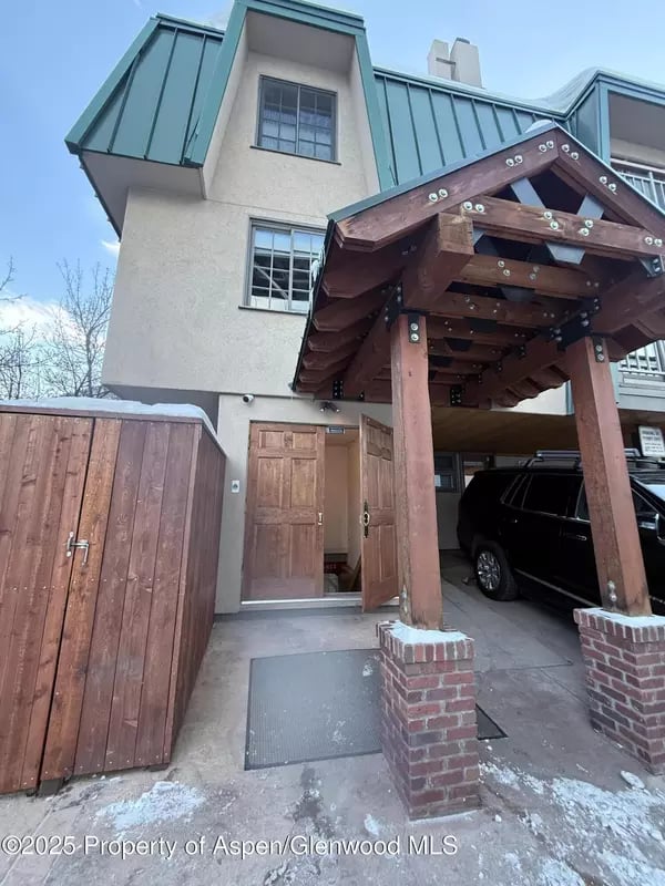 Home entrance with a timber porte-cochère, wooden gate, and black SUV parked beneath the cover.