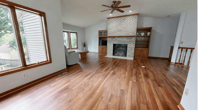 Living room with a white brick fireplace, built-in shelving, large windows, and warm wood floors.