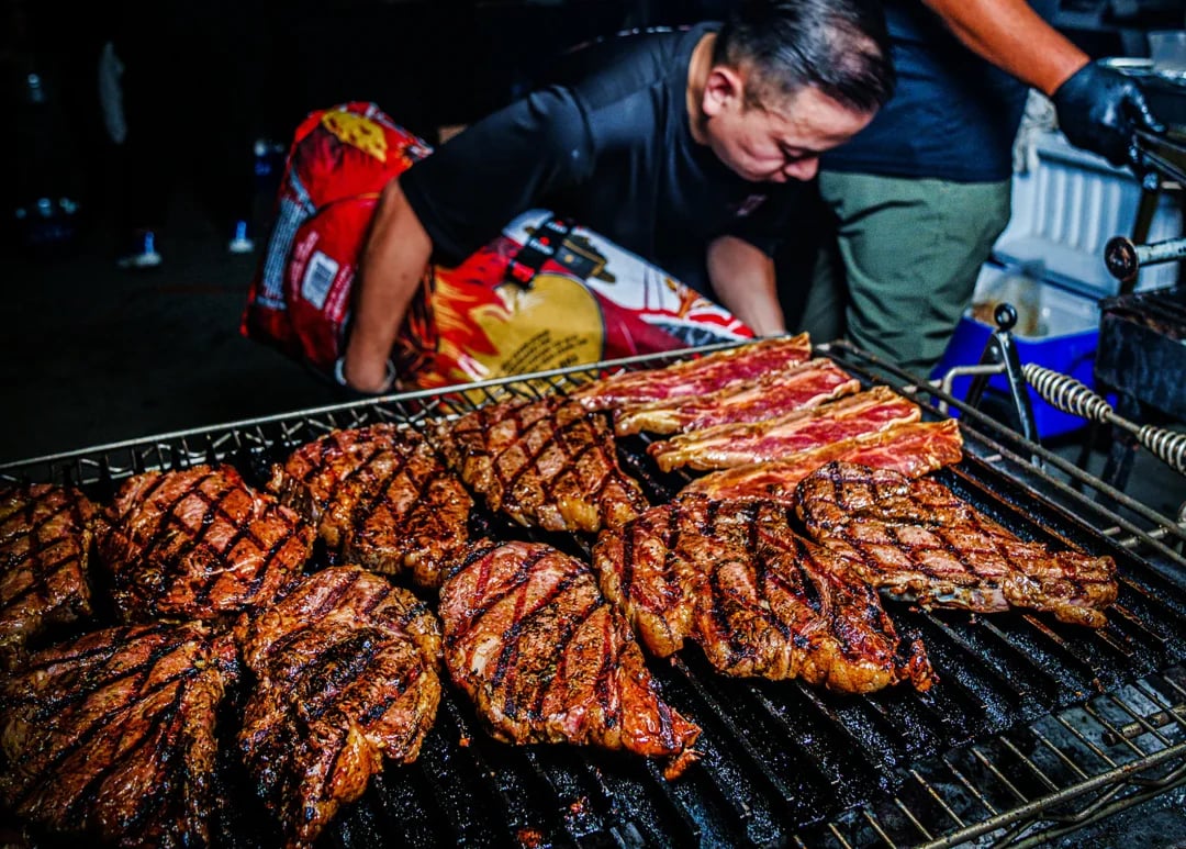 Grilled steaks with dark sear marks cooking on a large barbecue grill.