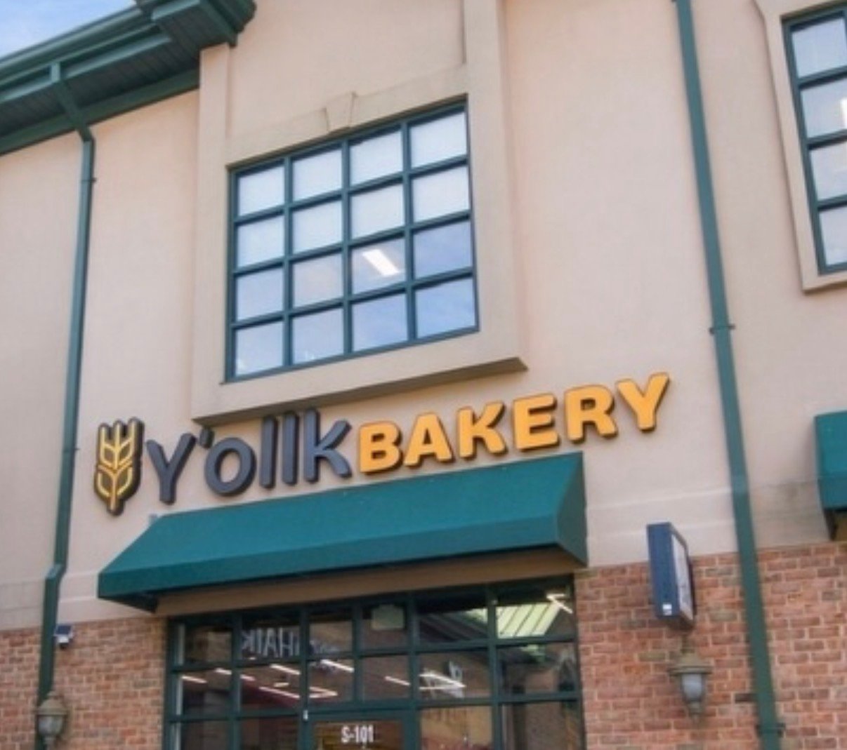 Y'olk Bakery storefront with gold lettering, teal awning, and brick lower facade.