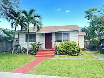 Single-story home with a red front door, red walkway, and palm trees in the front yard.