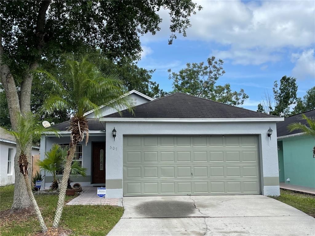 Single-story stucco house with a wide garage, concrete driveway, and palm trees in the front yard.