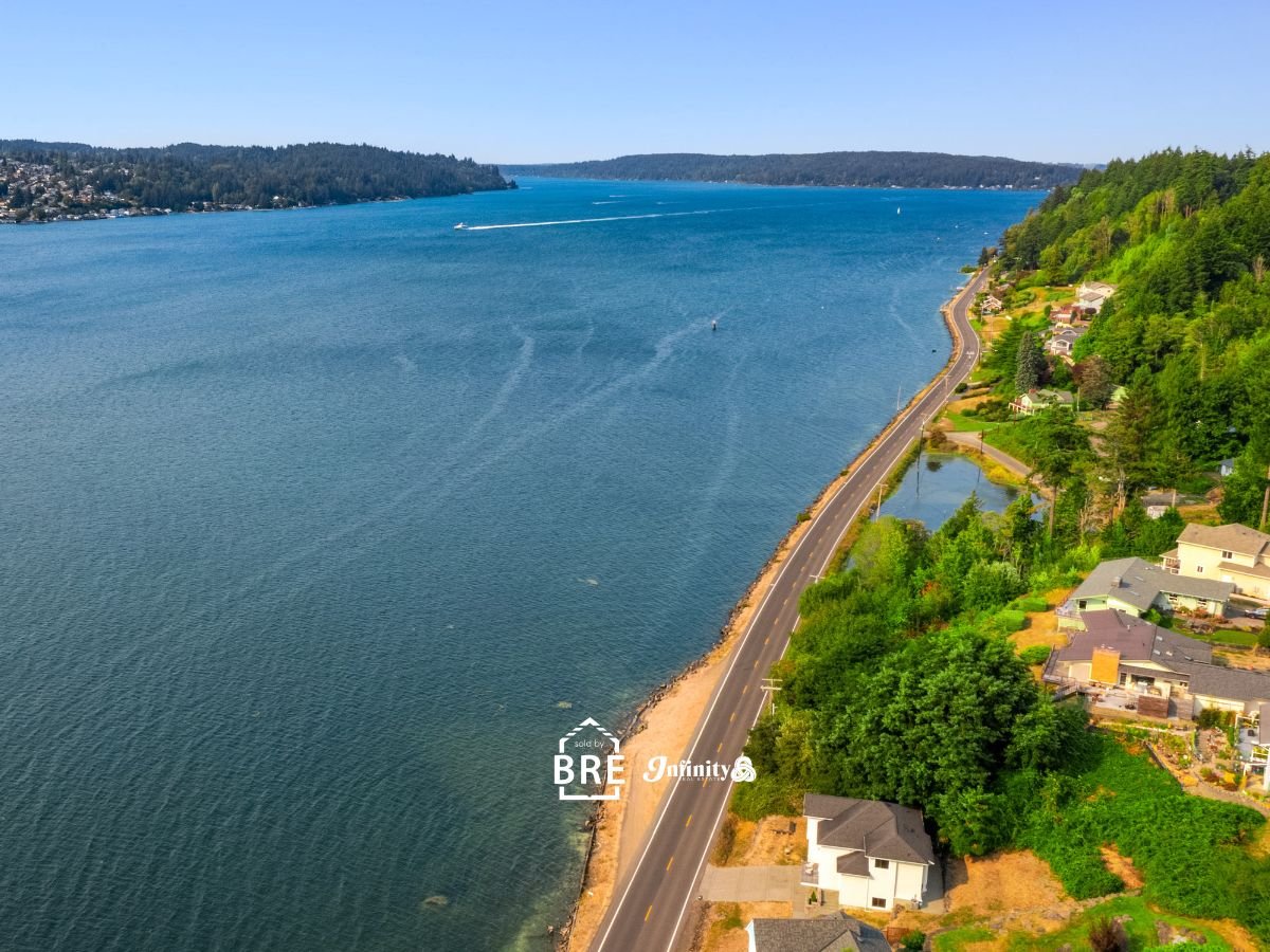 Aerial view of a blue bay beside a winding coastal road and wooded homes.