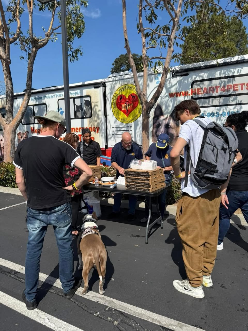 People gather around a table beside a Heart4Pets animal emergency vehicle, with a dog in the foreground.