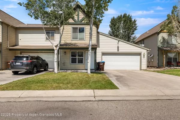 Two-story beige house with green trim, two garages, a driveway, and a small front lawn.