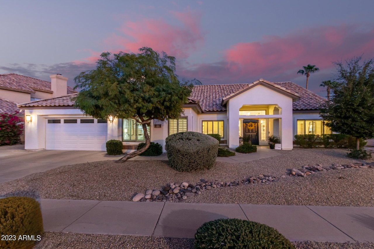 Single-story home with a tiled roof, two-car garage, and gravel landscaping beneath a pink dusk sky.