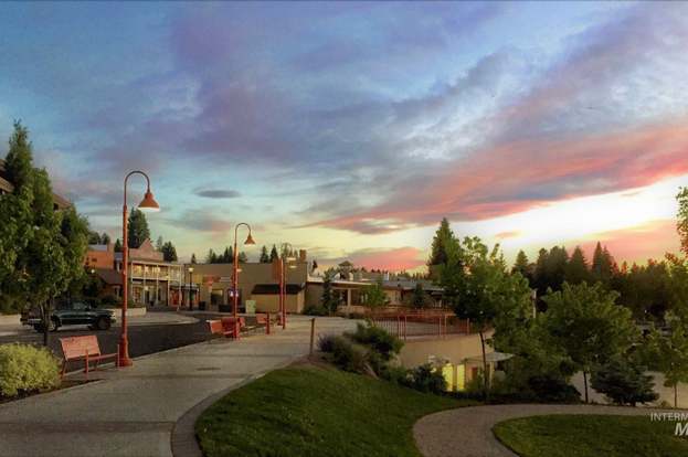 Downtown streetscape at sunset, with curved sidewalks, red streetlamps, trees, and storefronts.