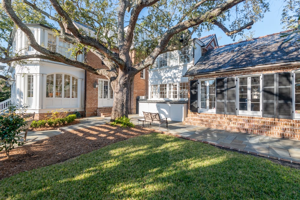 Brick-and-white home with a stone patio, lawn, and sprawling oak tree.