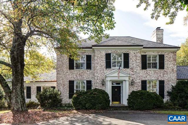 Two-story brick house with black shutters and a columned entrance beneath mature trees.