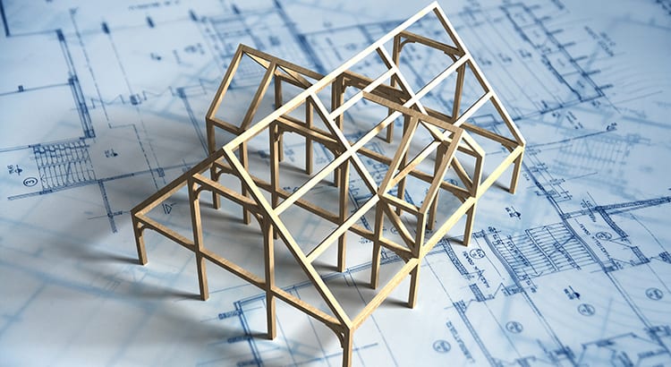 A miniature model of a house constructed with wooden sticks placed on top of blueprints. This image suggests planning or construction.