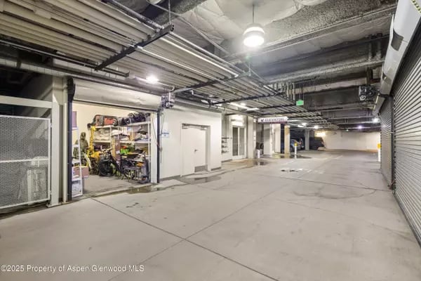 Indoor parking garage with exposed overhead utilities and a secured storage area.