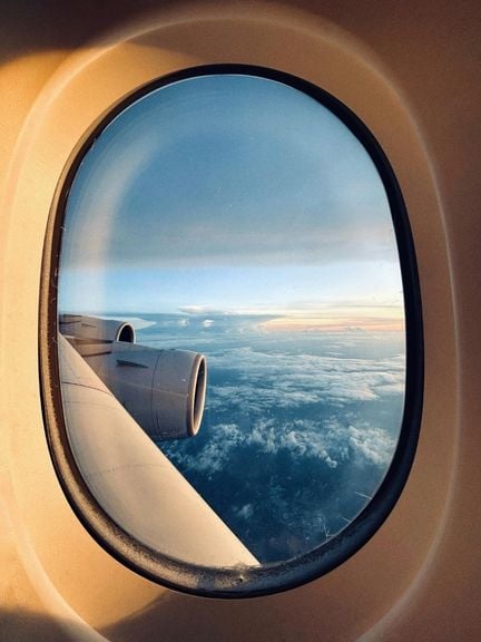 Airplane wing and engine above clouds, seen through a window at sunrise.