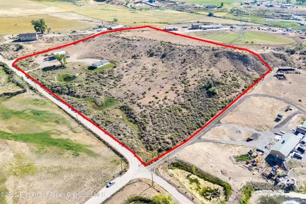 Aerial view of a scrub-covered land parcel outlined in red, bordered by roads and scattered buildings.