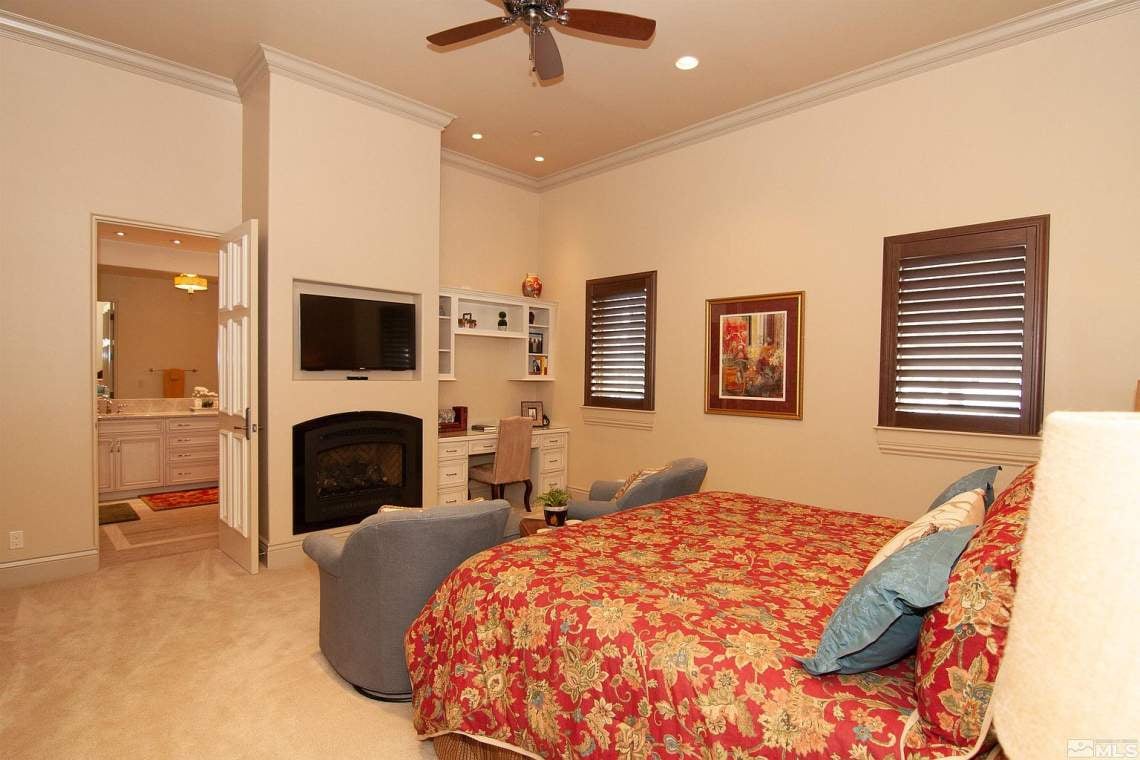 Bedroom with a red floral quilt, fireplace, and built-in desk and shelves.
