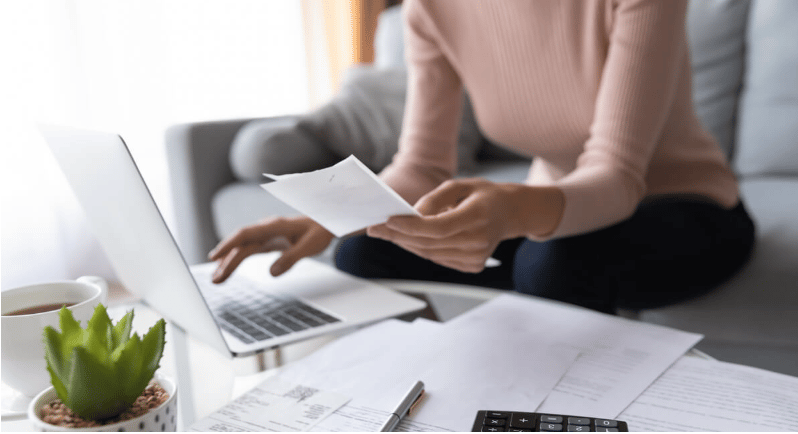 Person reviewing paperwork beside a laptop, with documents and a calculator on the table.