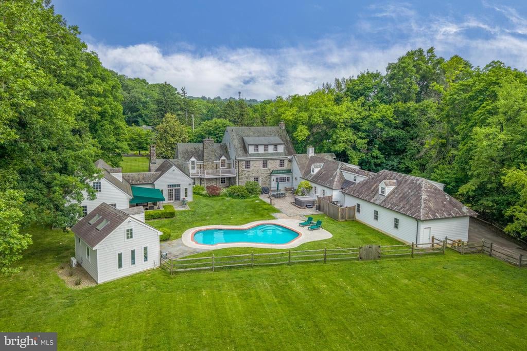 A wooded estate with several buildings surrounding a lawn and swimming pool.