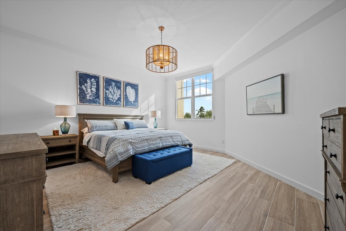Bright bedroom with a large bed, blue bench, and tall window overlooking palm trees.