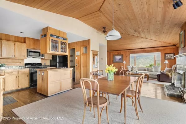 Open-plan dining room and kitchen with a vaulted wood ceiling and mountain views through the living room windows.