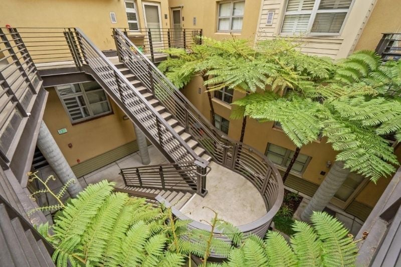 A view looking down at a spiral and straight staircase in the central courtyard of the Harbor Lofts, surrounded by greenery.