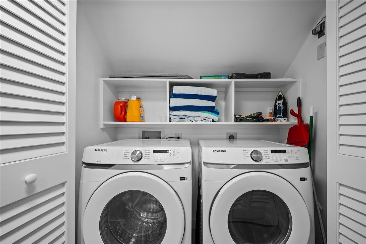 Laundry room with Samsung washer and dryer beneath shelves of folded towels and supplies.