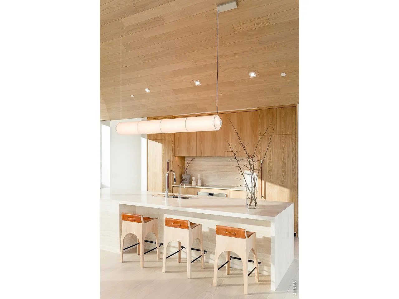 Modern kitchen with a white island, three wooden stools, and warm wood cabinetry.