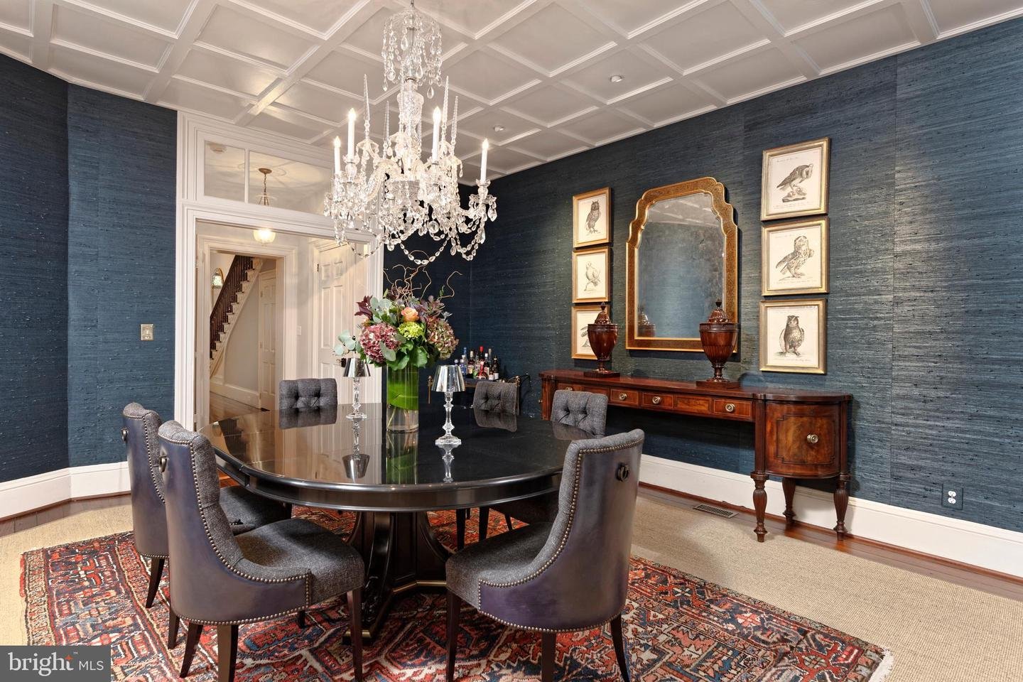 Dining room with a crystal chandelier, dark oval table, blue walls, and patterned rug.