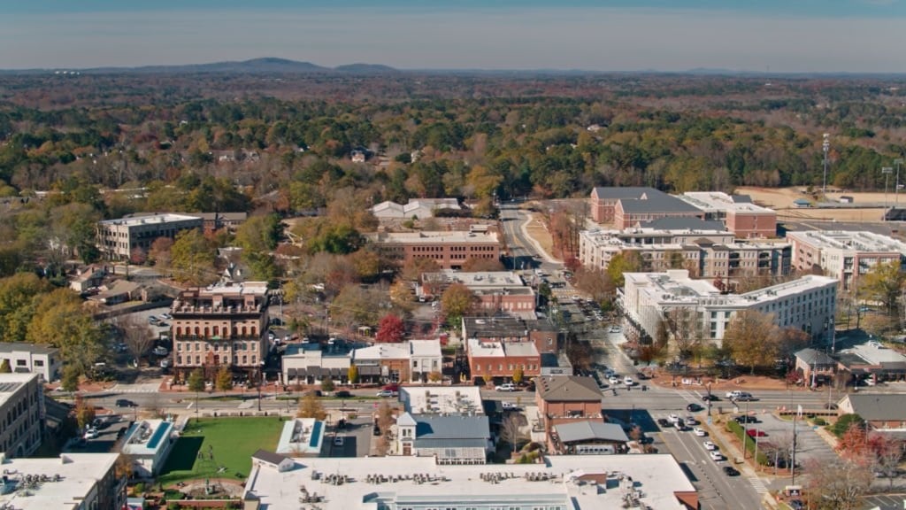 Aerial view of a town center surrounded by autumn-colored trees and distant hills.