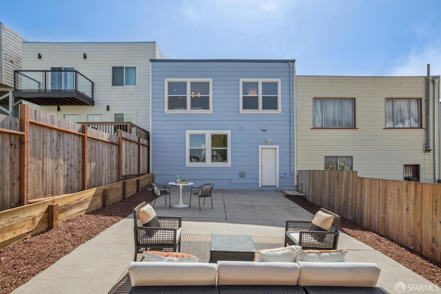 Fenced concrete patio behind a blue-sided home, staged with outdoor sofas, chairs, and a table.