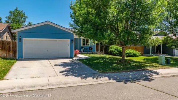 Blue single-story home with a wide garage door, concrete driveway, and leafy tree in the front yard.