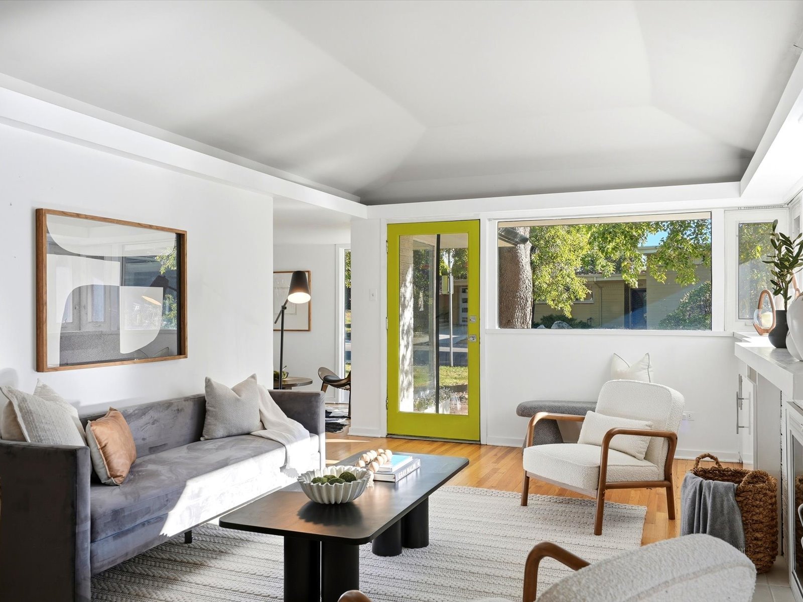 Living room with vaulted ceiling, gray sofa, wood floors, and a lime-green front door.
