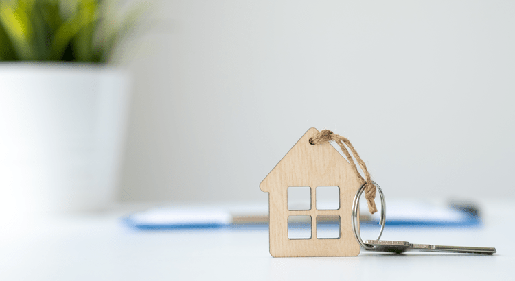 Wooden house-shaped key tag resting beside a metal key